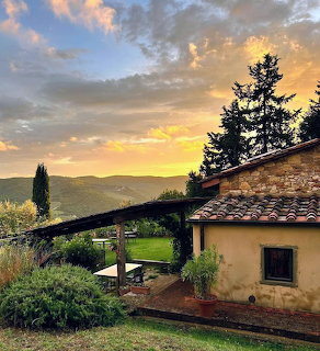 Rustic stone cottage with tiled roof, garden, and sunset sky in the countryside