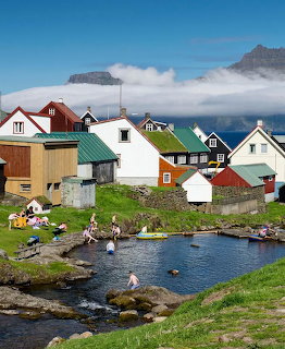 Colorful houses in Gjógv village with swimmers in natural pool and misty mountains behind