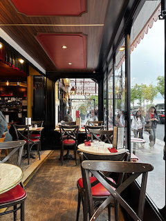 Interior view of a traditional Parisian café with red ceiling, bistro tables, chairs, and large street-facing windows