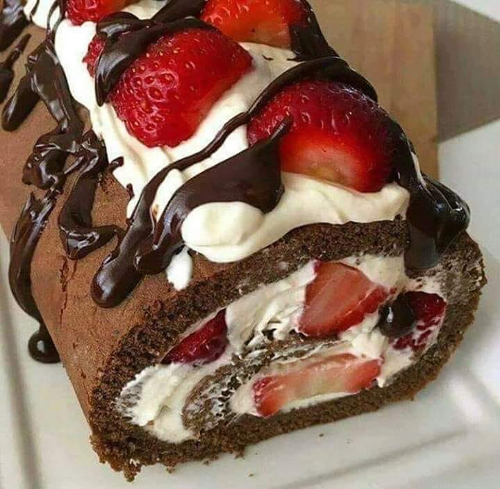 Chocolate cake roll slice with strawberries, cream filling, and chocolate drizzle on white plate