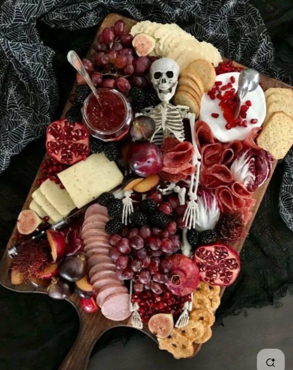 Halloween charcuterie board with cheese, meats, fruit, crackers, jam, and a small skeleton