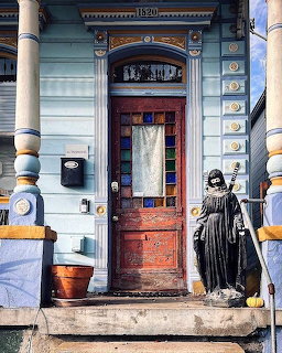 Blue vintage house exterior with arched wooden door, white columns, and statue figure on small front porch