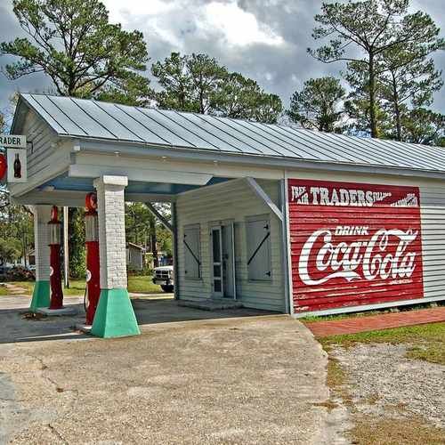 White vintage service station with red Coca-Cola sign and gas pumps under covered area