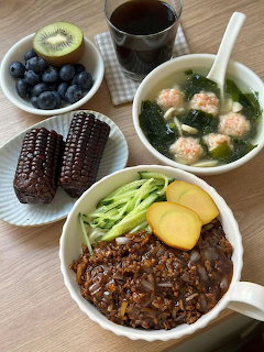 Top-down view of Korean-style dishes with black bean noodles, seaweed soup, corn, blueberries, and kiwi