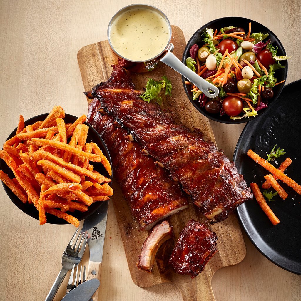 Barbecue ribs on a cutting board with sweet potato fries, salad, and sauce from above