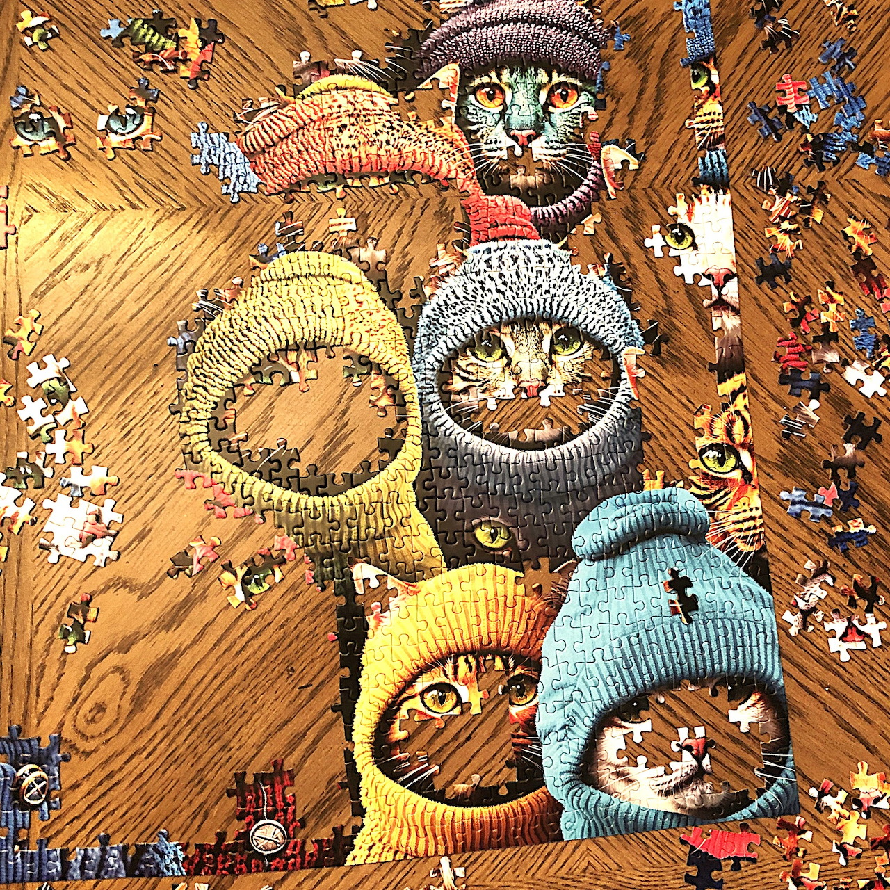 Four cats wearing colorful knitted sweaters on a wooden floor with scattered puzzle pieces