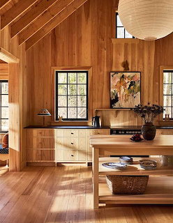 Modern kitchen interior with wood paneling, beamed ceiling, pendant light, and wooden island
