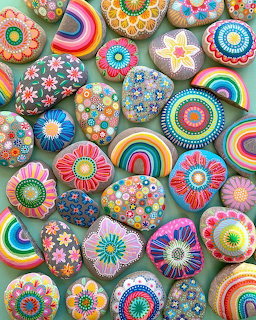Collection of hand-painted rocks with colorful mandala, flower, and rainbow designs arranged on white background