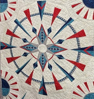 Symmetrical quilt with red and blue geometric spokes radiating from center on cream background
