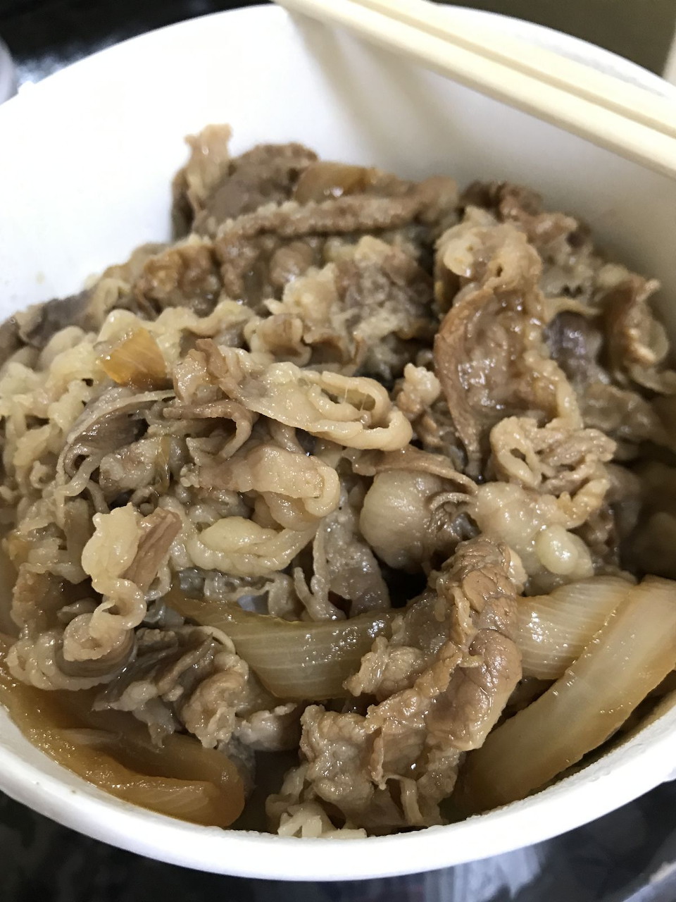Close-up of a gyudon beef bowl with sliced beef, onions, rice, and chopsticks