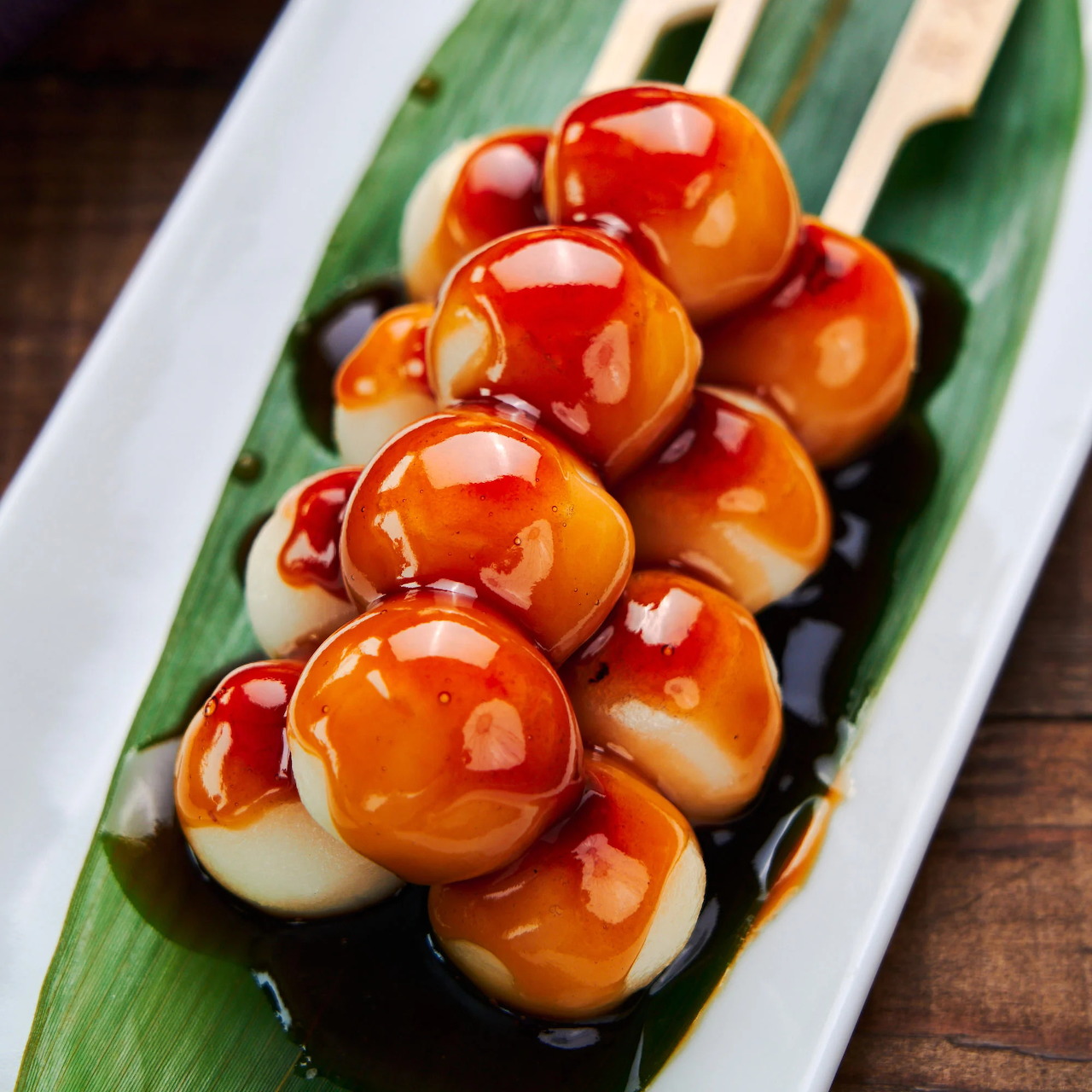 Mitarashi dango skewers with glossy brown soy glaze on a leaf-lined white plate