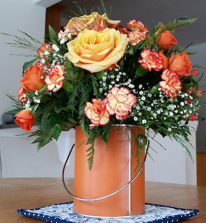 Peach roses and carnations with baby's breath in copper bucket vase on blue lace doily