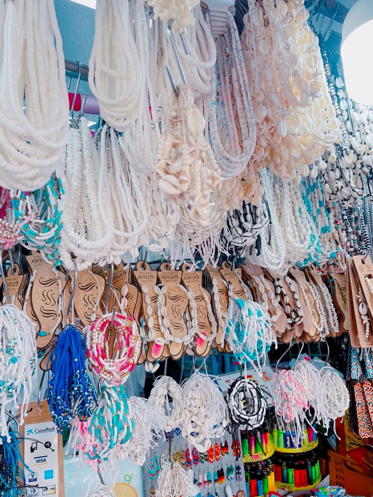 Market stall with rows of hanging white beaded necklaces, shell jewelry, and colorful accessories
