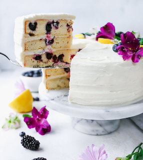 White frosted blueberry layer cake with a sliced piece on a marble stand