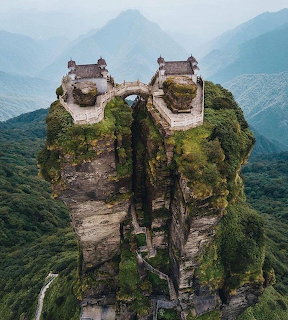 Two temples on rocky twin peaks of Fanjingshan mountain connected by bridge, surrounded by misty mountain ranges