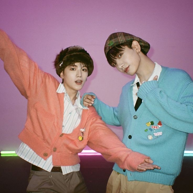Two young men posing in pastel cardigans against a purple studio backdrop