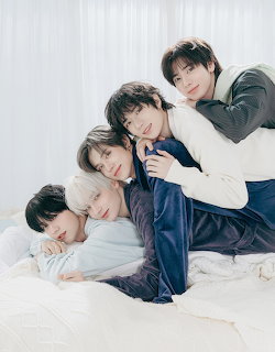 Five young men in slepwear cuddling together on a white bed in a studio photo