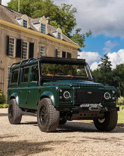 Green Land Rover Defender SUV parked in front of a stone manor house with cloudy sky