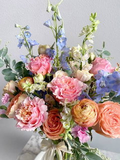 Colorful pastel flower bouquet with pink peonies, peach ranunculus, blue delphiniums and greenery in a vase