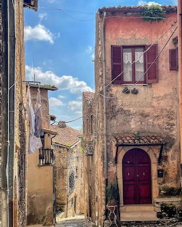 Narrow alley in Sermoneta Italy with old pink stone buildings, arched door, and hanging laundry