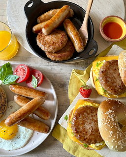 Breakfast table with eggs, sausages, pancakes, burgers, orange juice and syrup arranged on white surface