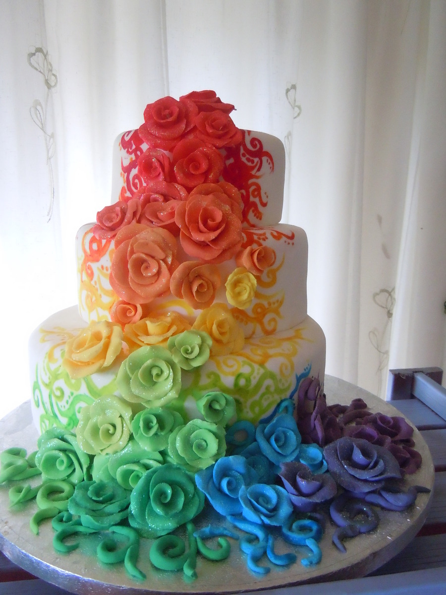 Three-tier white cake covered with rainbow roses and colorful fondant swirls