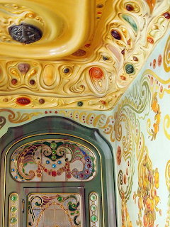 Ornate Art Nouveau ceiling with golden scrollwork and colorful details above a stained glass door