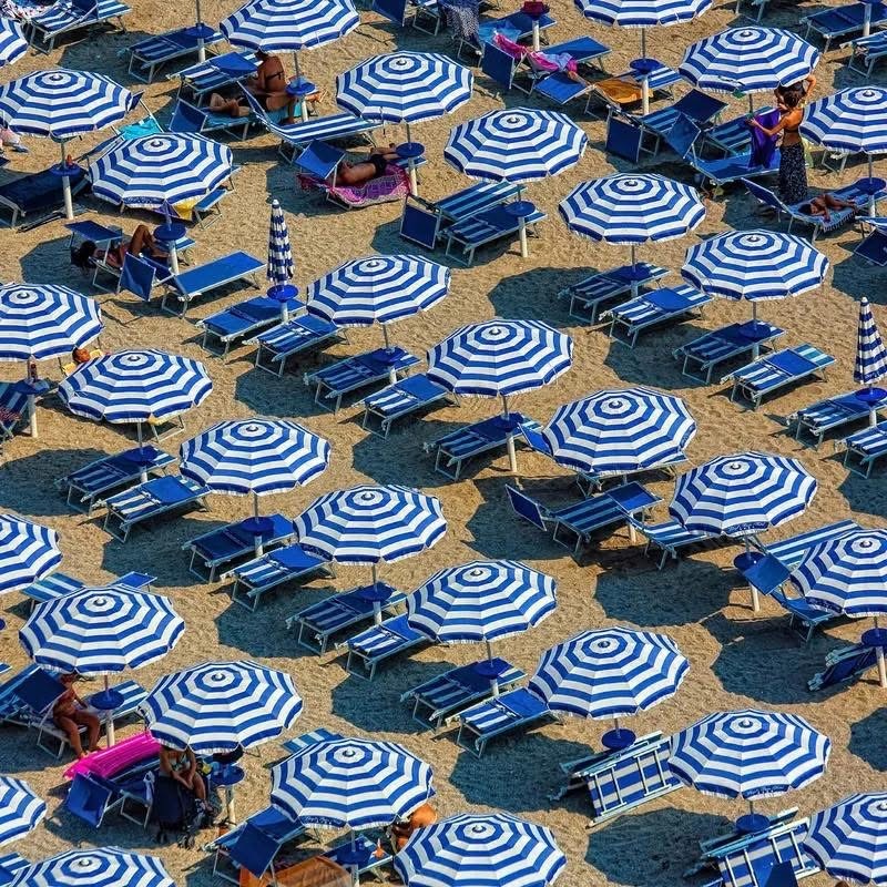 Overhead view of Italian beach with blue striped umbrellas and beach chairs arranged on sand