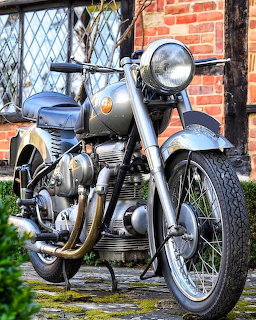 Vintage Sunbeam S7 motorcycle with chrome details parked by brick cottage