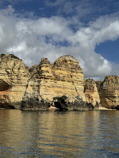 Golden layered sandstone cliffs along ocean coastline with blue sky and clouds