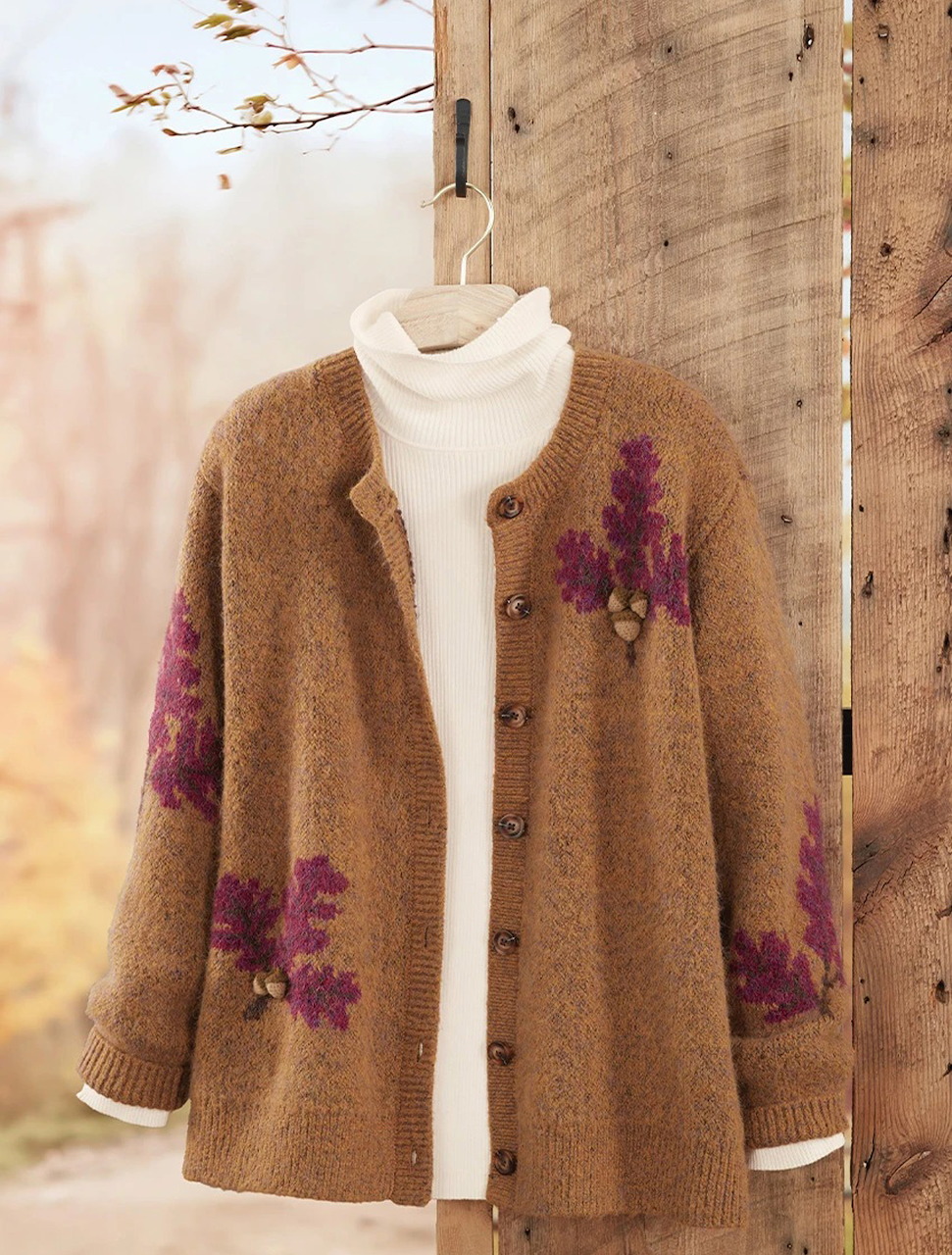 Brown knit cardigan with purple floral motifs and a cream turtleneck hanging on a wooden wall.