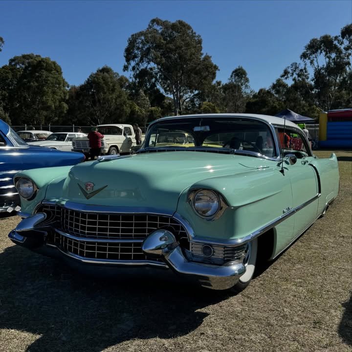 Mint green vintage Cadillac parked on grass at an outdoor car show