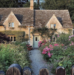 Stone cottage behind a gravel path lined with pink flowers and dense garden plants