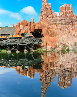 Big Thunder Mountain Railroad train passing red rock spires reflected in still water