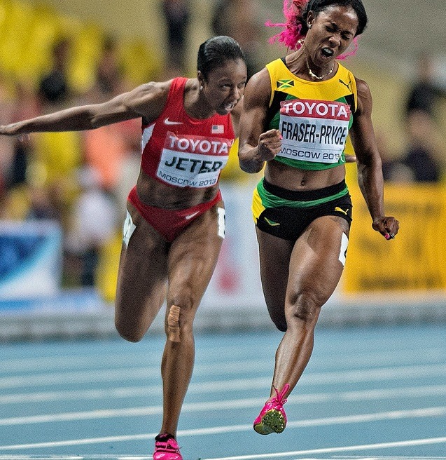 Two female sprinters racing on a blue athletics track