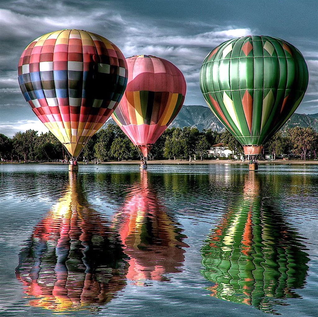 Three hot air balloons reflected in calm water with stormy sky background