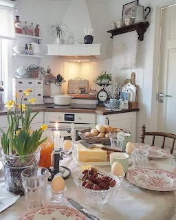 Cozy cottage kitchen with white walls, open shelving, dining table with flowers and fruit bowls