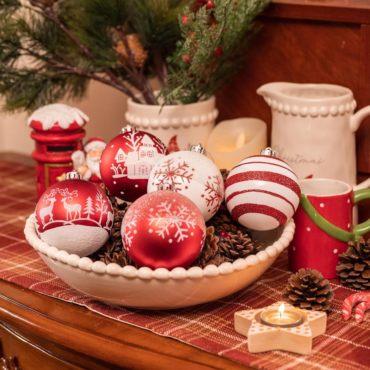 Wooden bowl filled with red and white Christmas ornaments on decorated table with greenery and pinecones