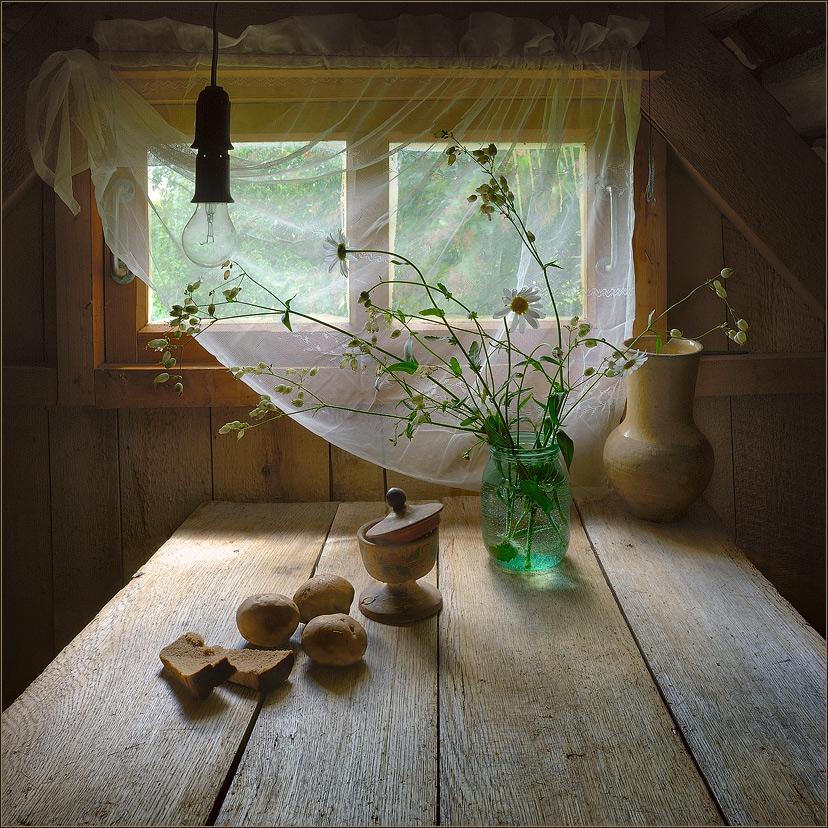 White wildflowers in a glass vase on a rustic wooden table by a softly lit window