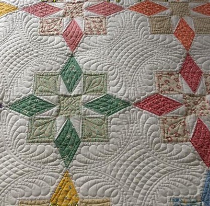 Close-up of a pastel quilt with diamond and square geometric patchwork pattern and decorative quilting stitches