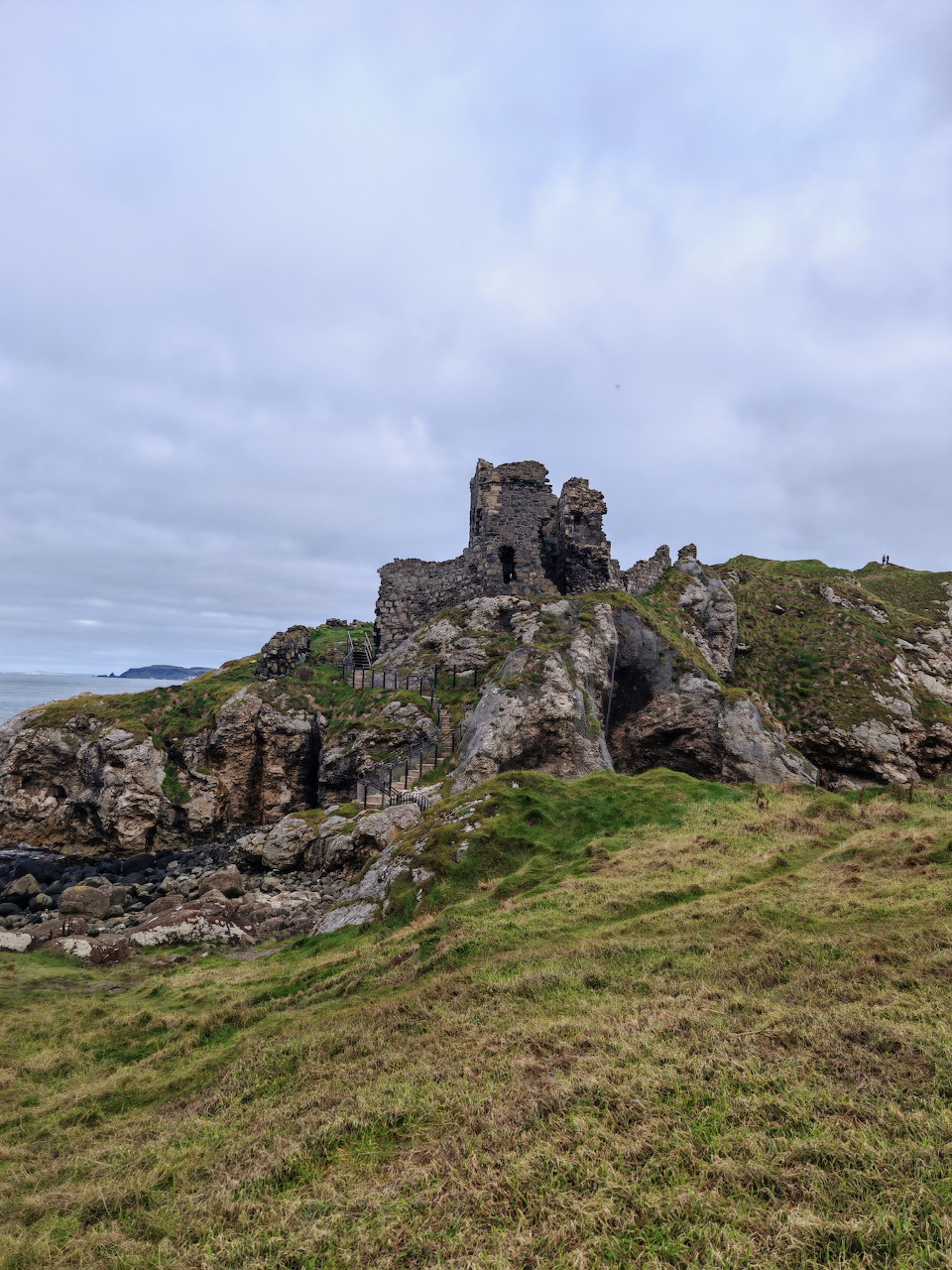 Ruins of Kinbane Castle on rocky coastal cliffs with green grass and grey overcast sky, Northern Ireland