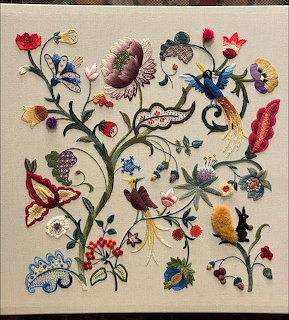 Colorful crewel embroidery with flowers, butterflies, and birds on cream linen fabric
