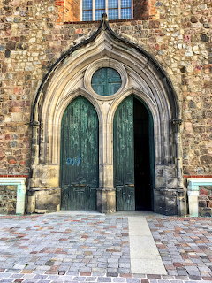 Ornate Gothic arched doorway with green wooden doors in weathered stone church wall