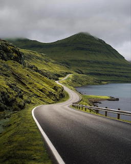 Winding road along a green mountain beside a fjord with cloudy skies