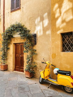 Yellow Vespa scooter parked on a cobblestone Italian street next to a wooden door with climbing plants