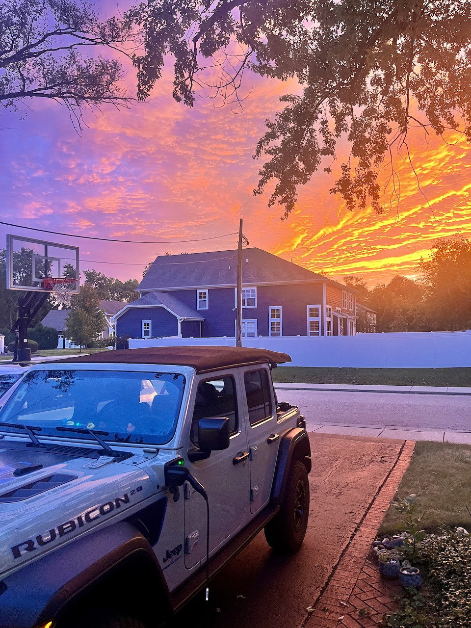 White Jeep Wrangler Rubicon in a driveway under a vivid orange and purple sunset sky