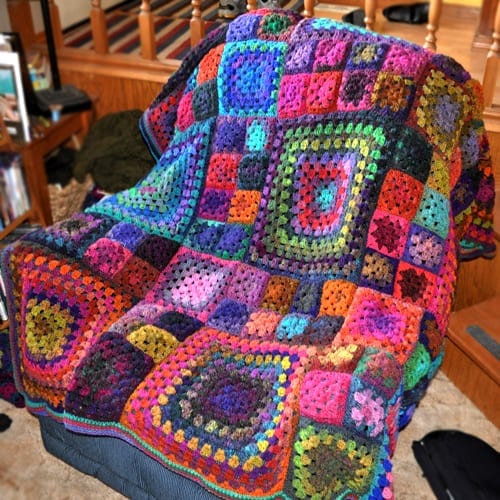 Colorful crochet granny square blanket draped over a chair indoors