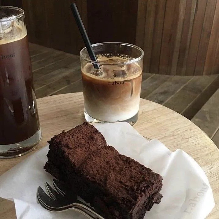 Brownie on a white plate with two iced coffee drinks on a wooden cafe table