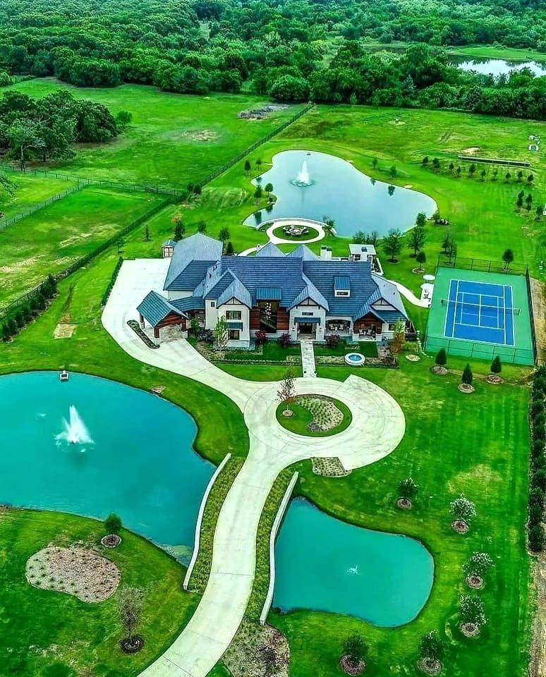 Aerial photo of a luxury mansion with ponds, fountains, tennis court, and expansive green grounds