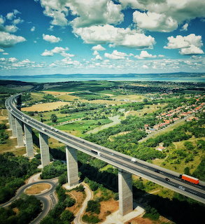 Elevated highway viaduct over green countryside beneath a blue sky with white clouds